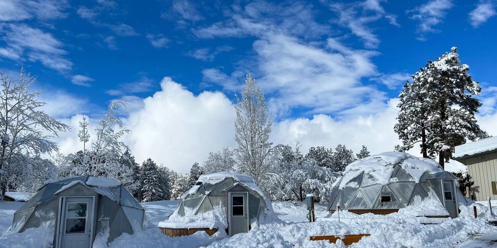 Three Growing Dome Greenhouses covered with snow and blue sky in background