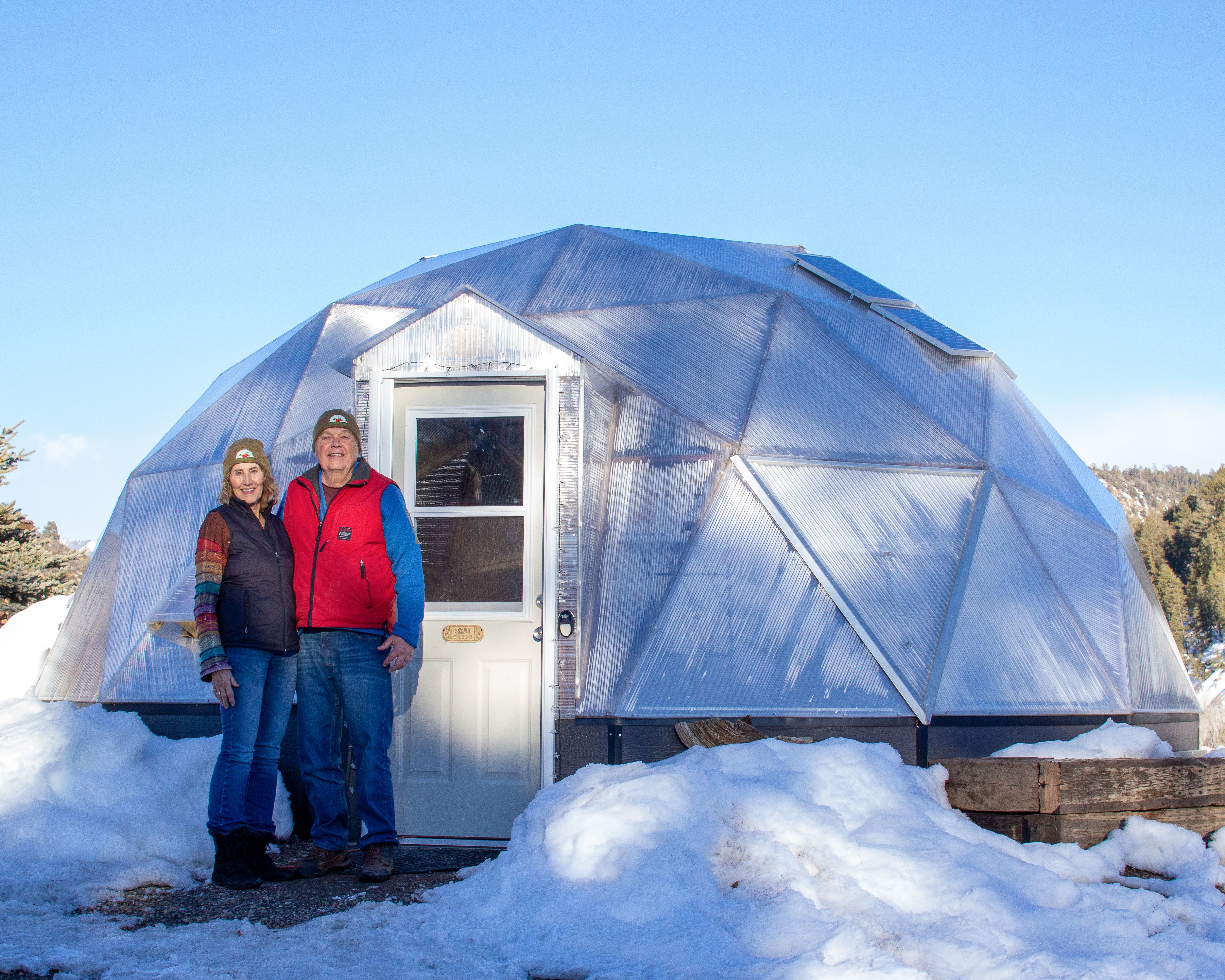 A couple standing in front of their Growing Dome greenhouse with snow surrounding