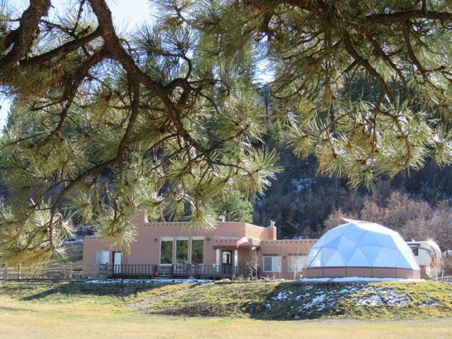 Growing Dome greenhouse with a stucco foundation wall, shown next to a residential home.