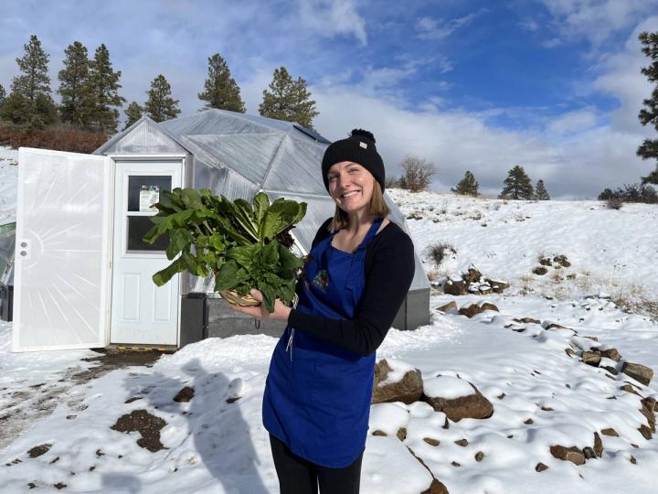 woman holding winter crops like greens and kales in a snowy landscape with a geodesic greenhouse in the background