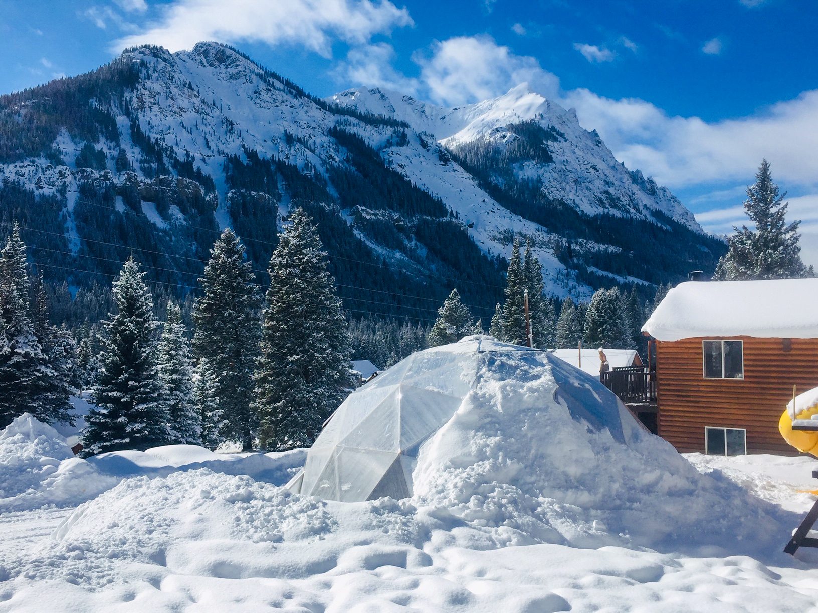 large deep winter greenhouse with snow banked up on one side and mountain peaks in the background