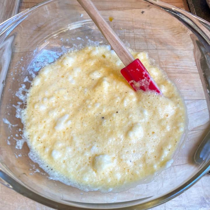 egg batter in a clear bowl on a butcher block with a red silicone spatula in the bowl