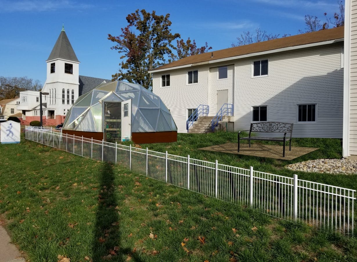 growing dome greenhouse near white clapboard buildings in late summer