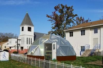growing dome greenhouse near white clapboard buildings in late summer