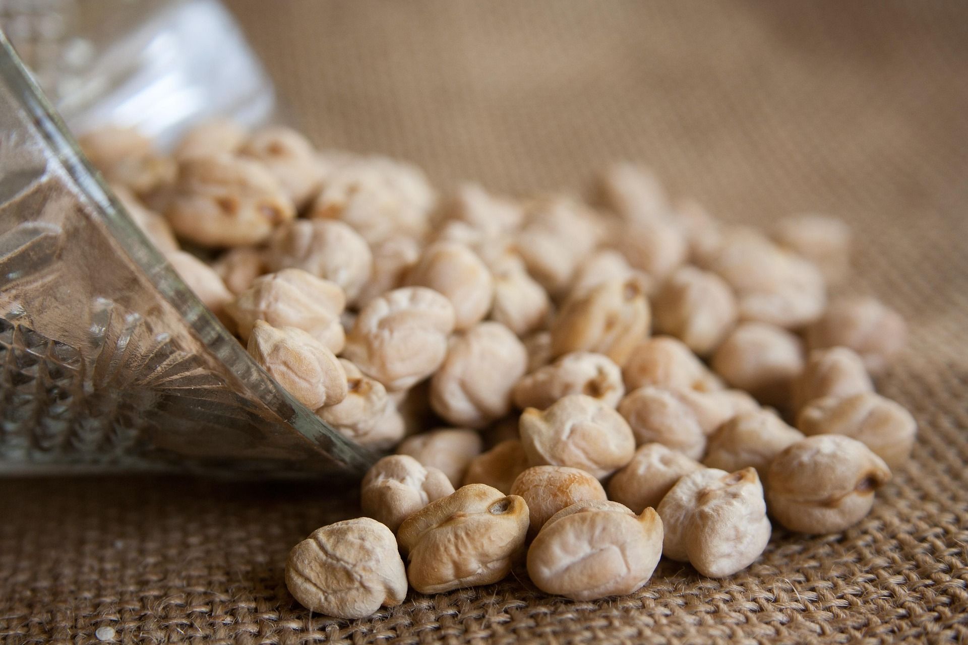 dried chickpeas spilling out of a glass bowl onto a burlap mat