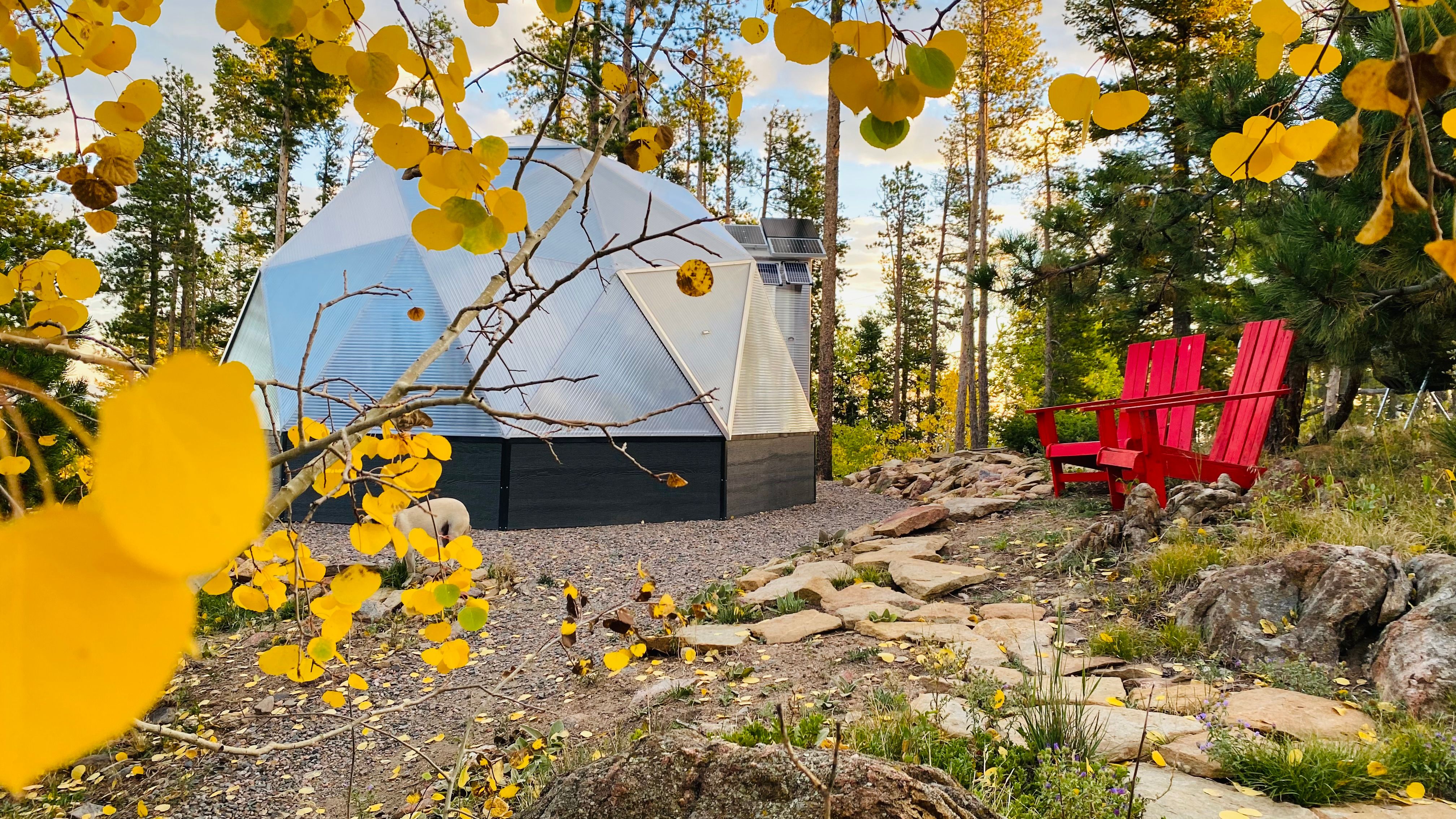 golden aspen leaves frame 18 foot diameter geodesic greenhouse with red adirondack chairs outside
