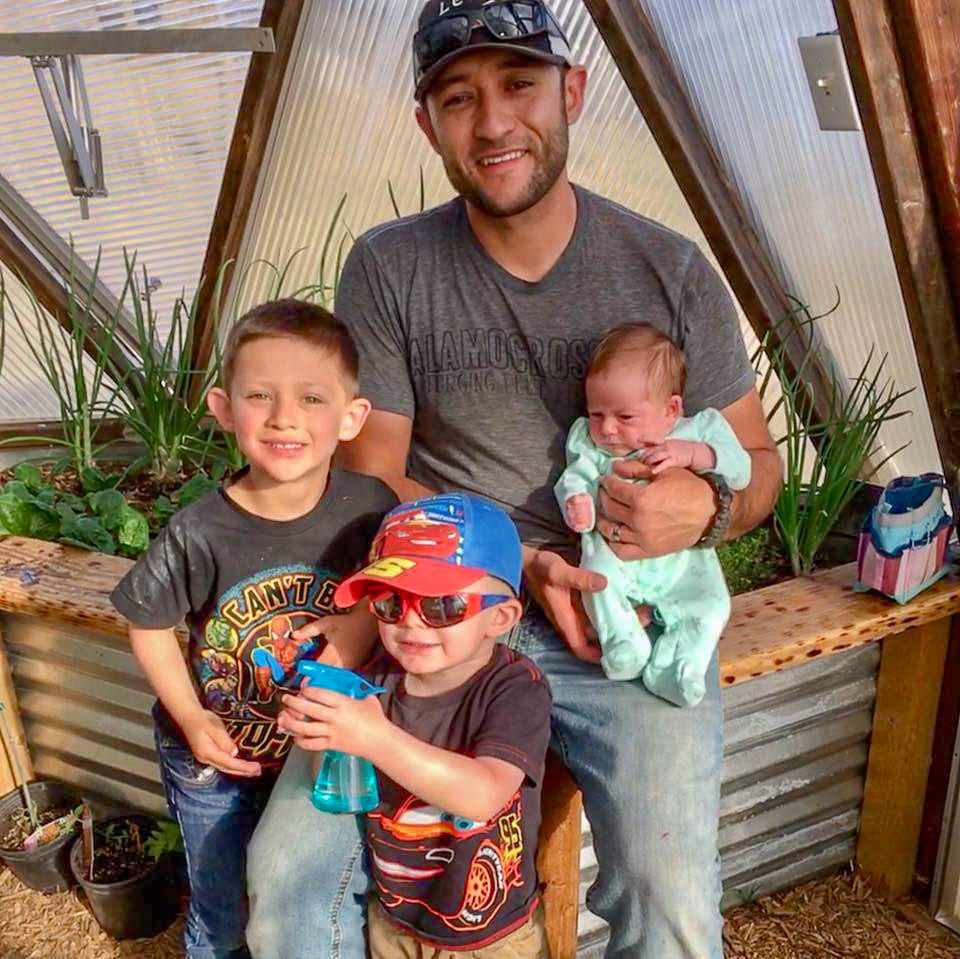 Man with three young children posing for a photo in a greenhouse