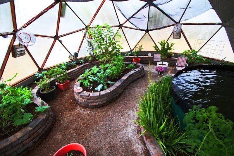 looking down on the pond and stone raised beds inside a growing dome greenhouse