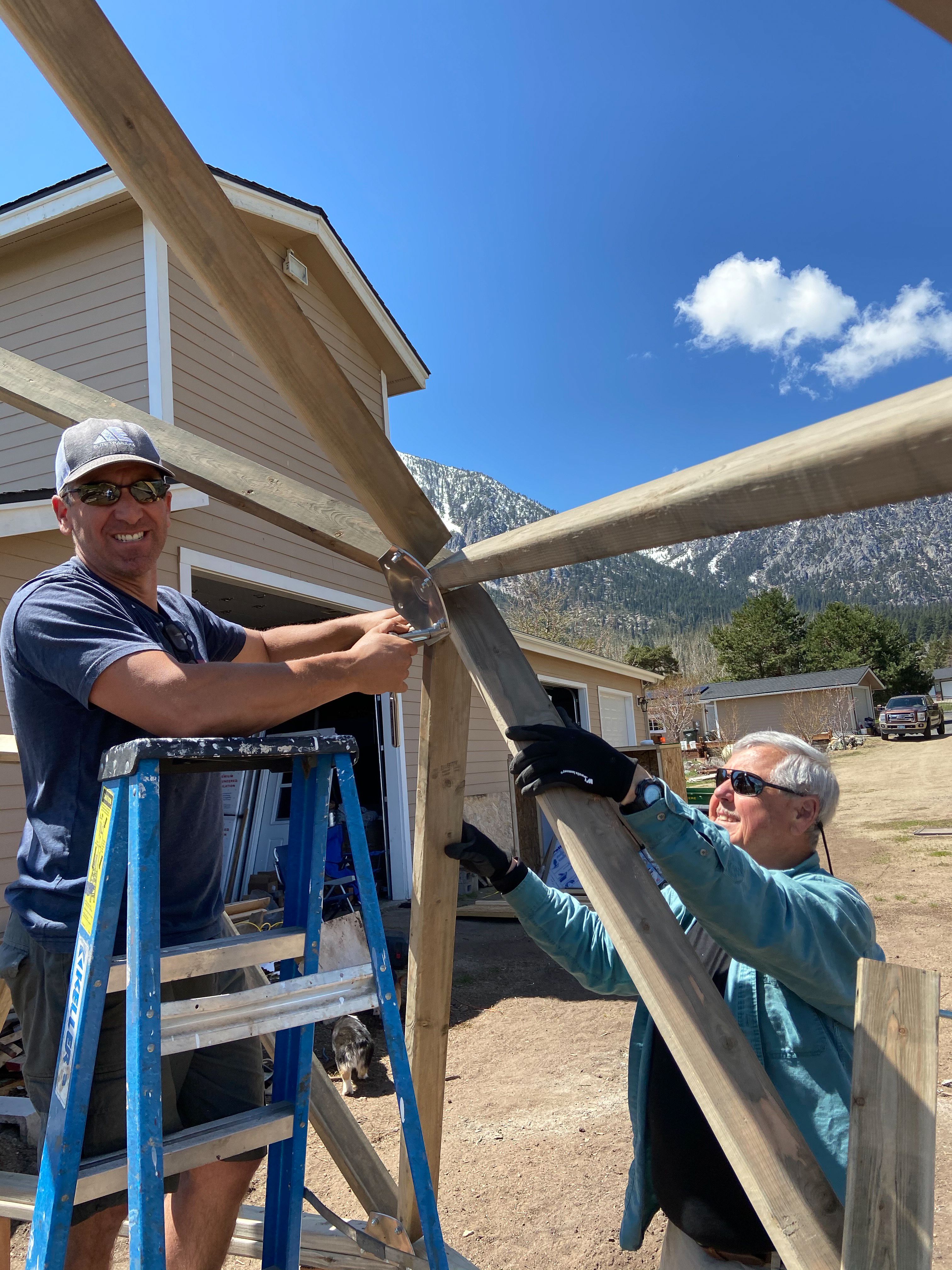 Two men building a geodesic greenhouse one is on a ladder and the other on the ground