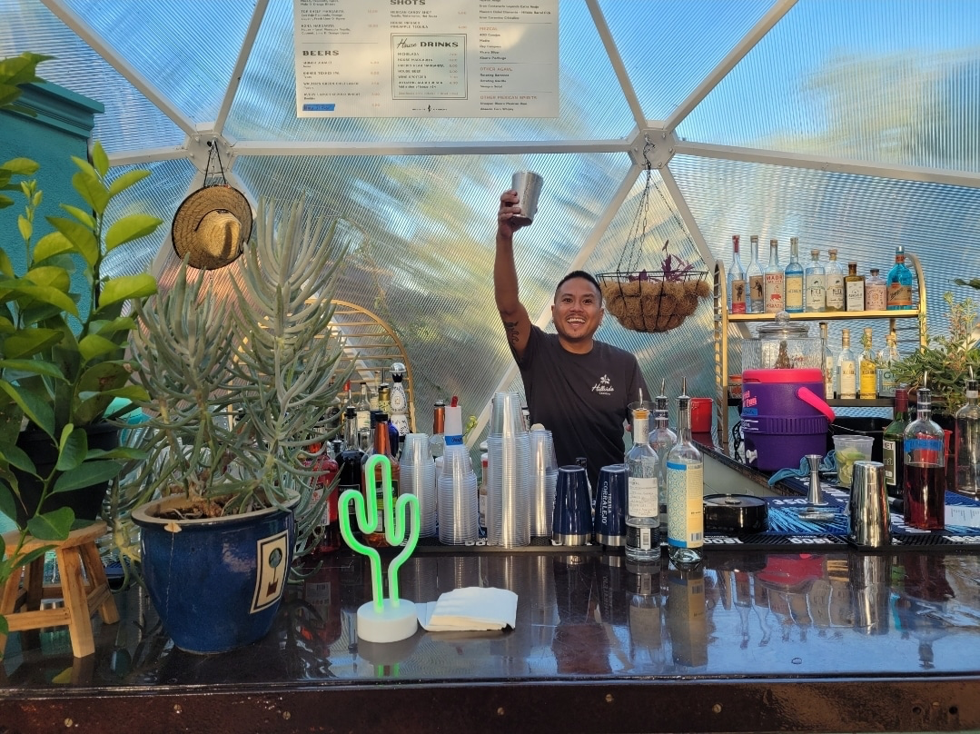Bartender raising a glass behind a bar inside a Growing Dome greenhouse