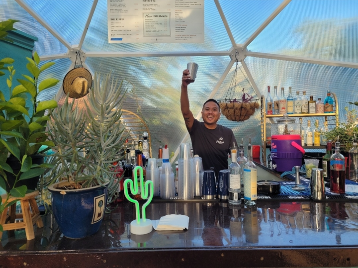 Bartender raising a glass behind a bar inside a Growing Dome greenhouse