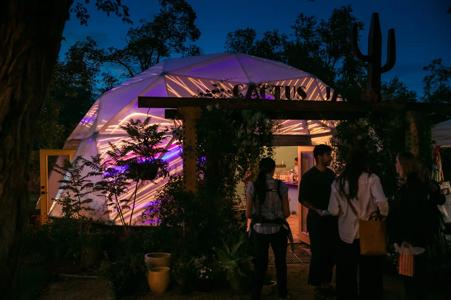 Growing Dome greenhouse illuminated purple and orange at night with people outside