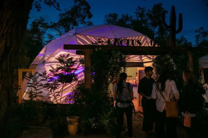 Growing Dome greenhouse illuminated purple and orange at night with people outside