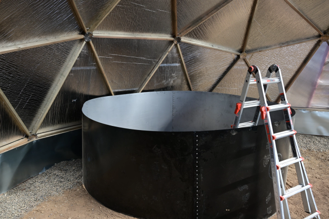 sheet metal formed into a circle for the above-ground pond with a ladder set in it inside the greenhouse