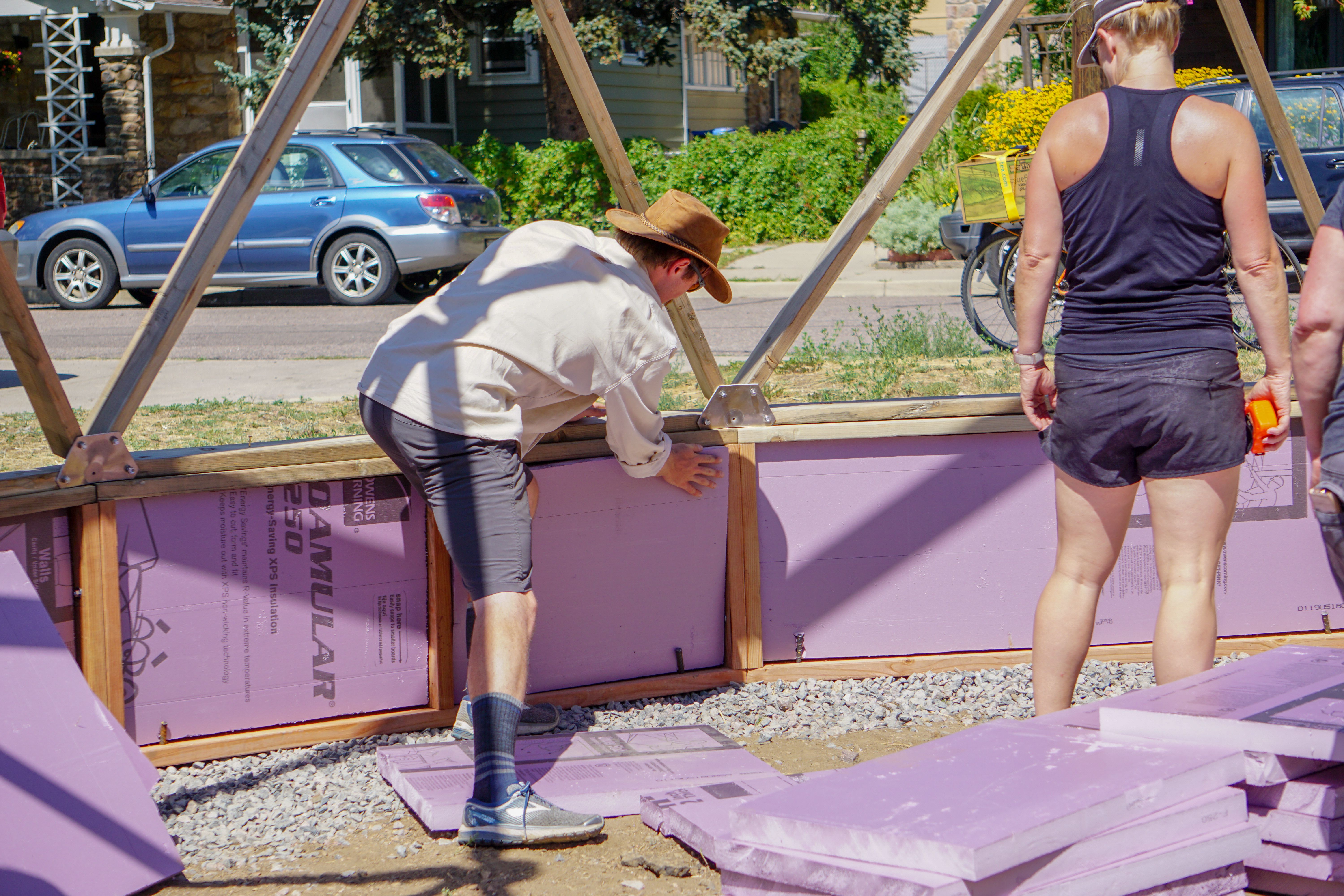 person installing rigid insulation in the cavity of the greenhouse foundation wall