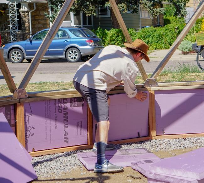 person installing rigid insulation in the cavity of the greenhouse foundation wall