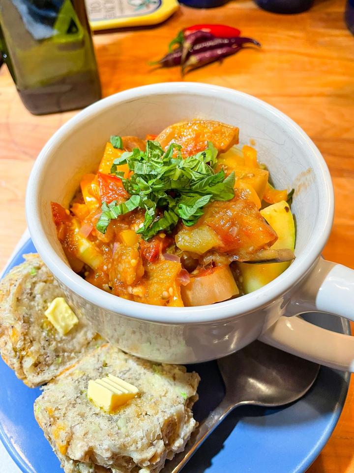ratatouille serving suggestion, in a bowl topped with fresh basil with a zucchini muffin on the side