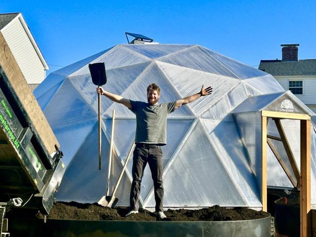 Grower filling an outdoor raised bed beside a Growing Dome in Medford, Massachusetts