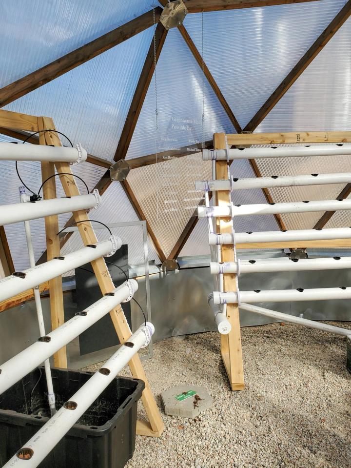 2 homemade vertical aquaponic towers with 5 and 6 white pvc tubes oriented horizontally at slight angles to allow water to flow from the top pipe, through the middle pipes, and down to the bottom