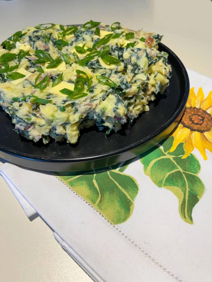 Colcannon plated on a black plate with green onions sprinkled on top and a sunflower napkin
