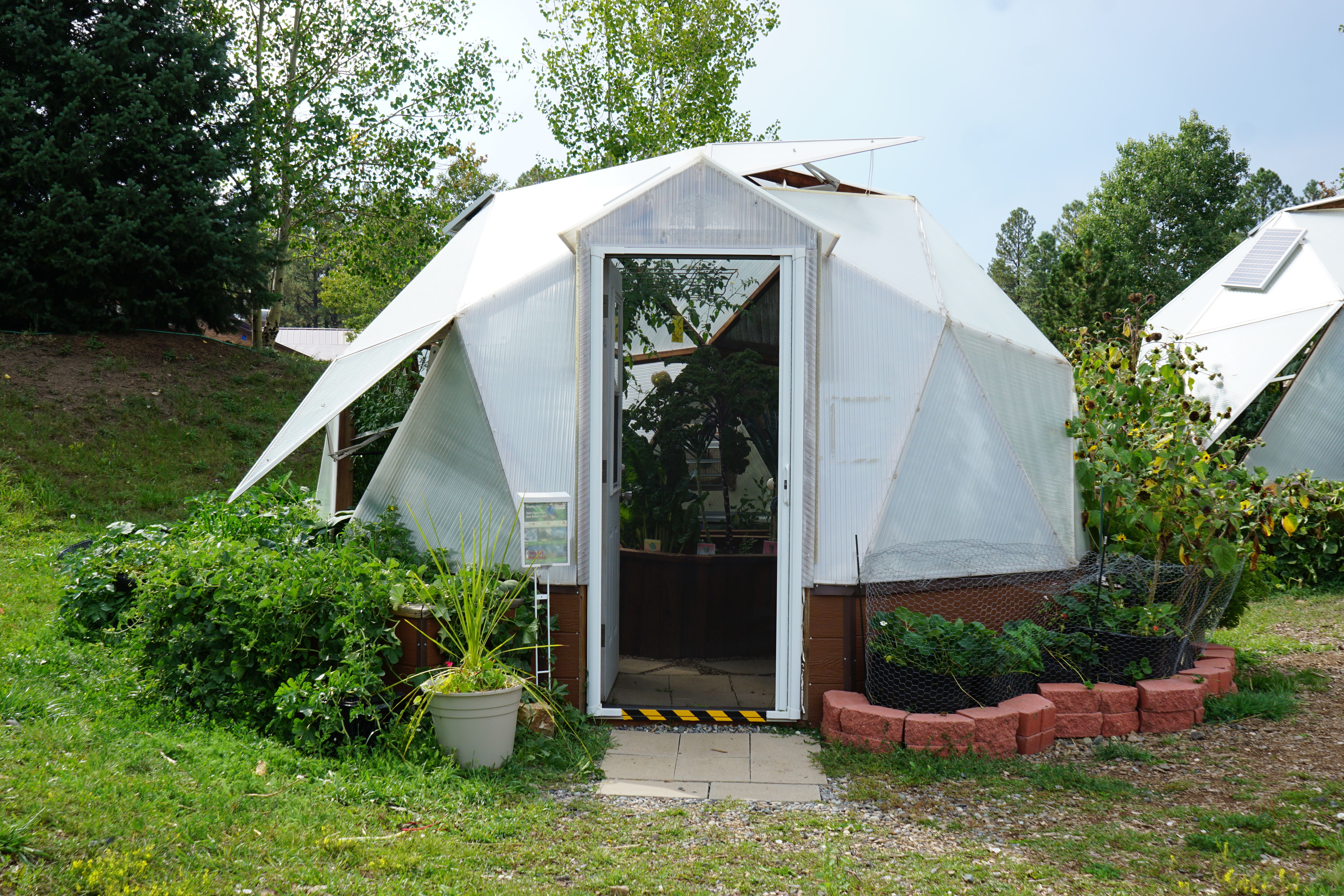 Growing Dome with an open door surrounded by garden beds and trees