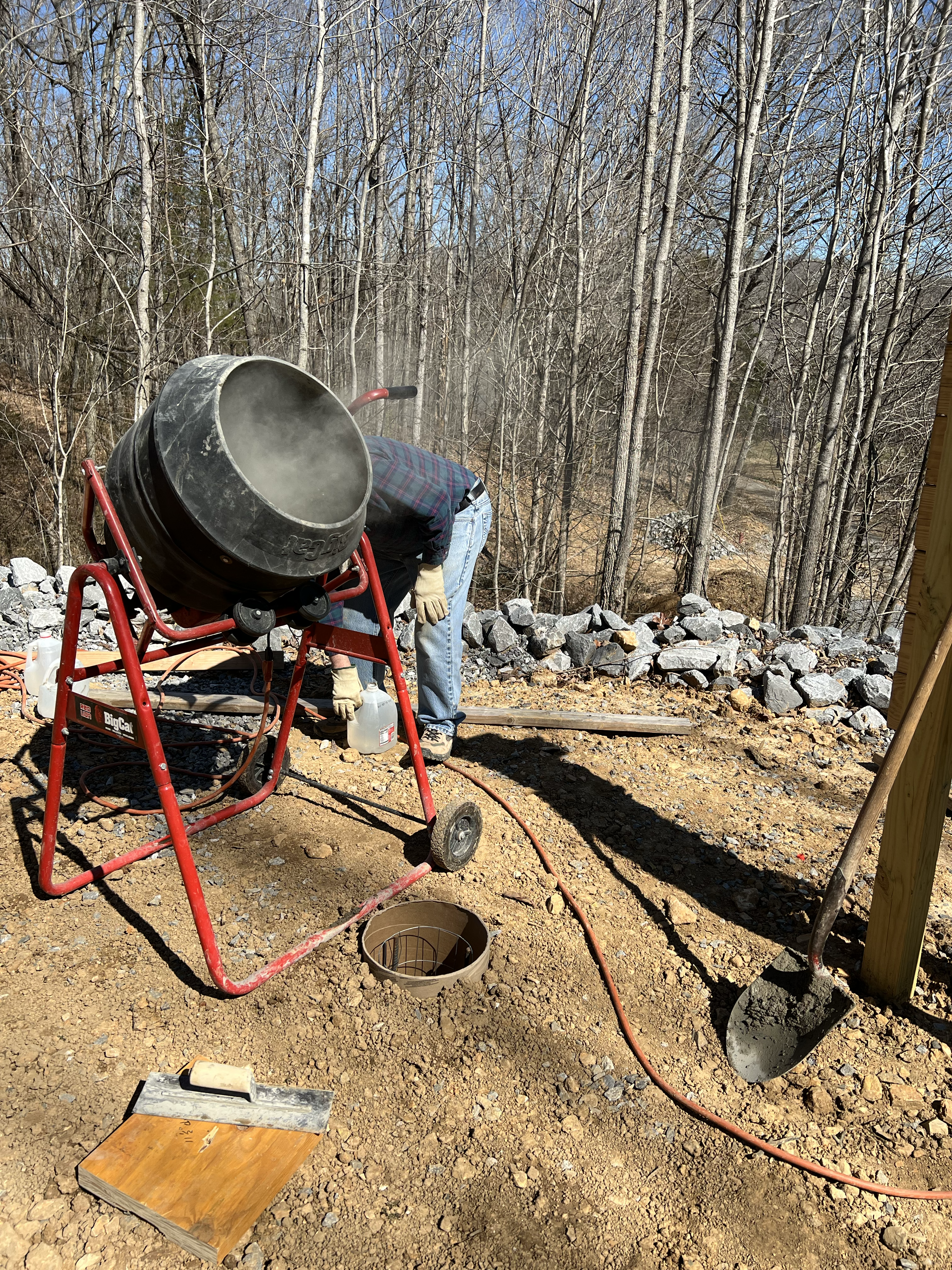person preparing concrete in a mixer to pour piers for a greenhouse