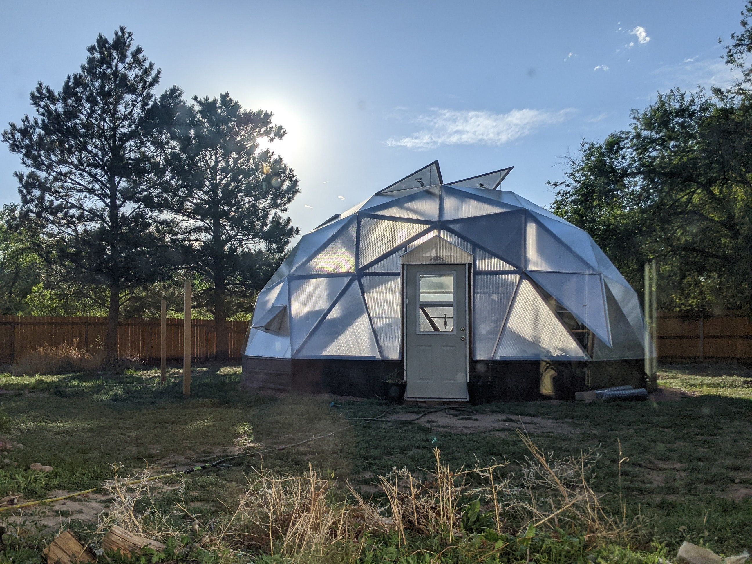 Growing Dome greenhouse backlit by sun in a fenced yard