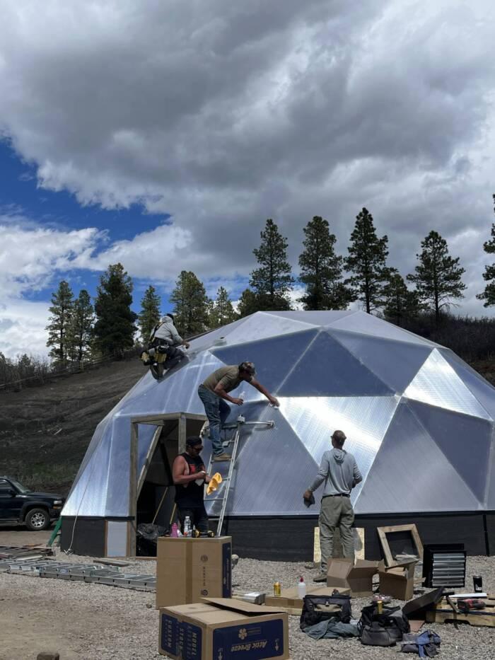 Full crew installation of a 33 foot growing dome with various boxes of parts and components in foreground and 4 men working