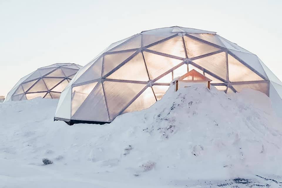 twin 42 foot growing dome greenhouses covered in snow at sunrise