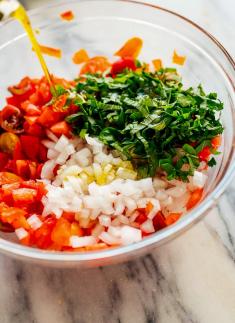 adding olive oil to bruschetta vegetables in a bowl
