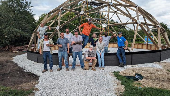 ReEntry program volunteers posing in front of heir half built dome greenhouse as a team