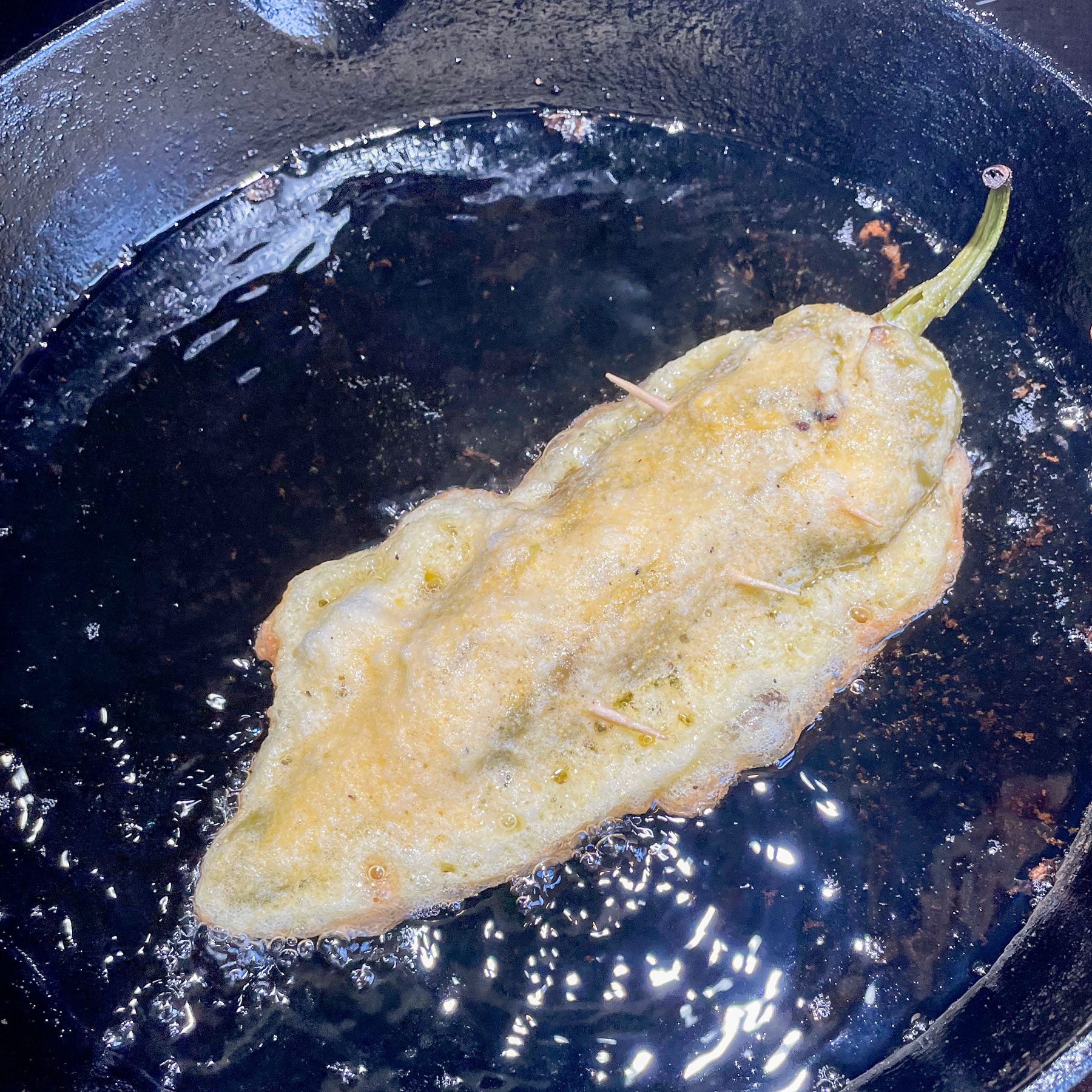 chile relleno frying in a cast iron skillet, the side facing up is still raw batter