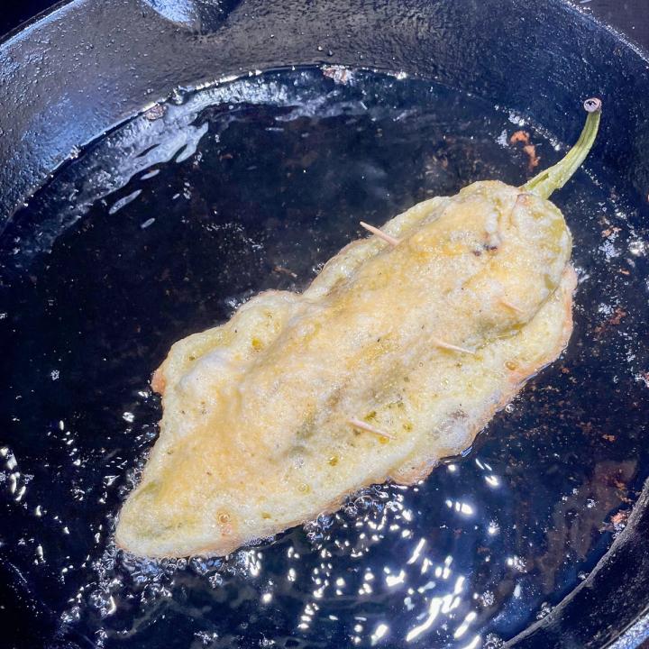 chile relleno frying in a cast iron skillet, the side facing up is still raw batter