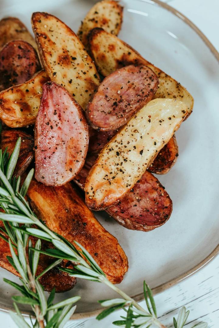 Growing sweet potato recipe, plate of cooked and spiced potatoes with a sprig of rosemary
