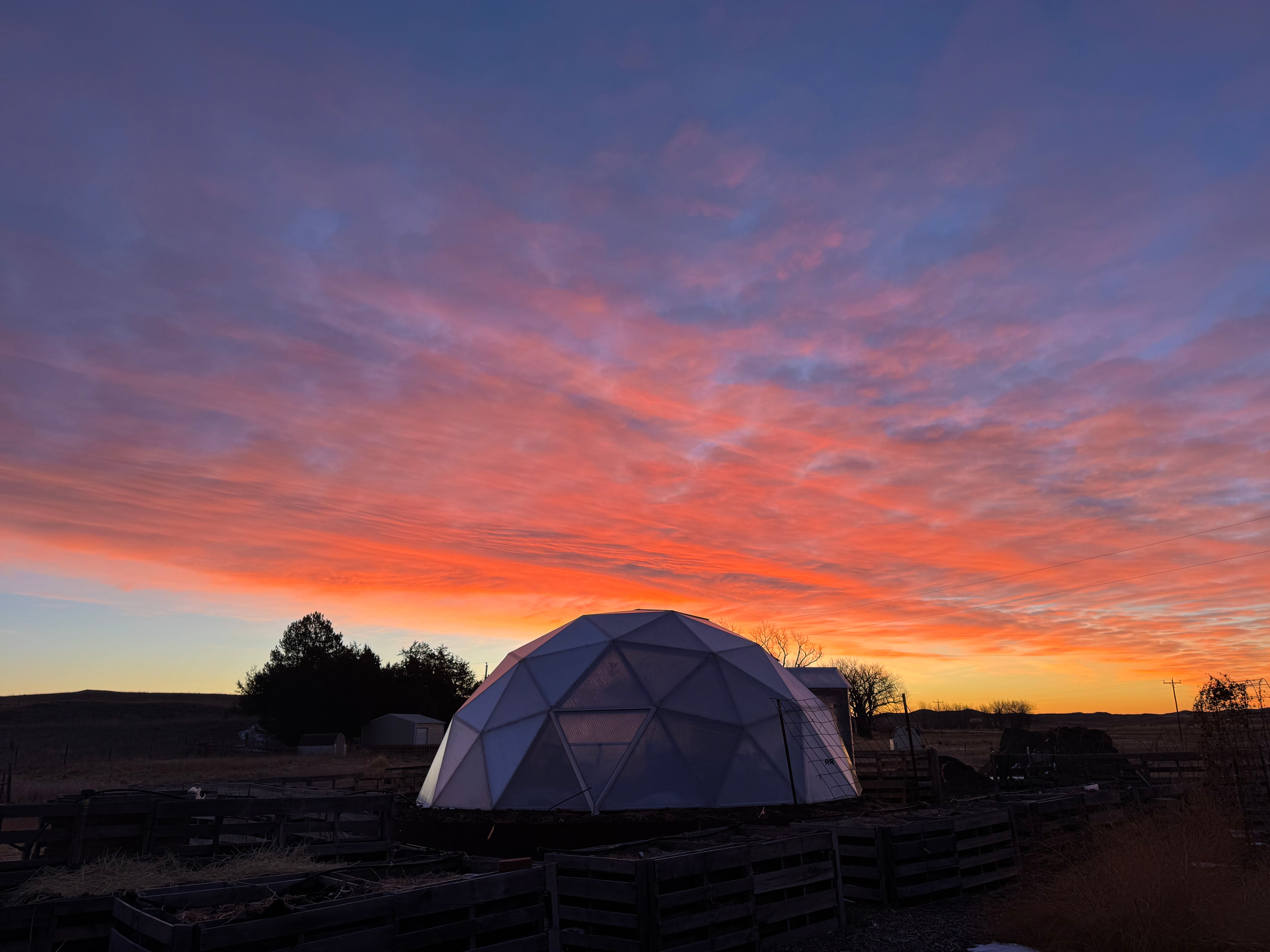 sun setting behind a growing dome greenhouse