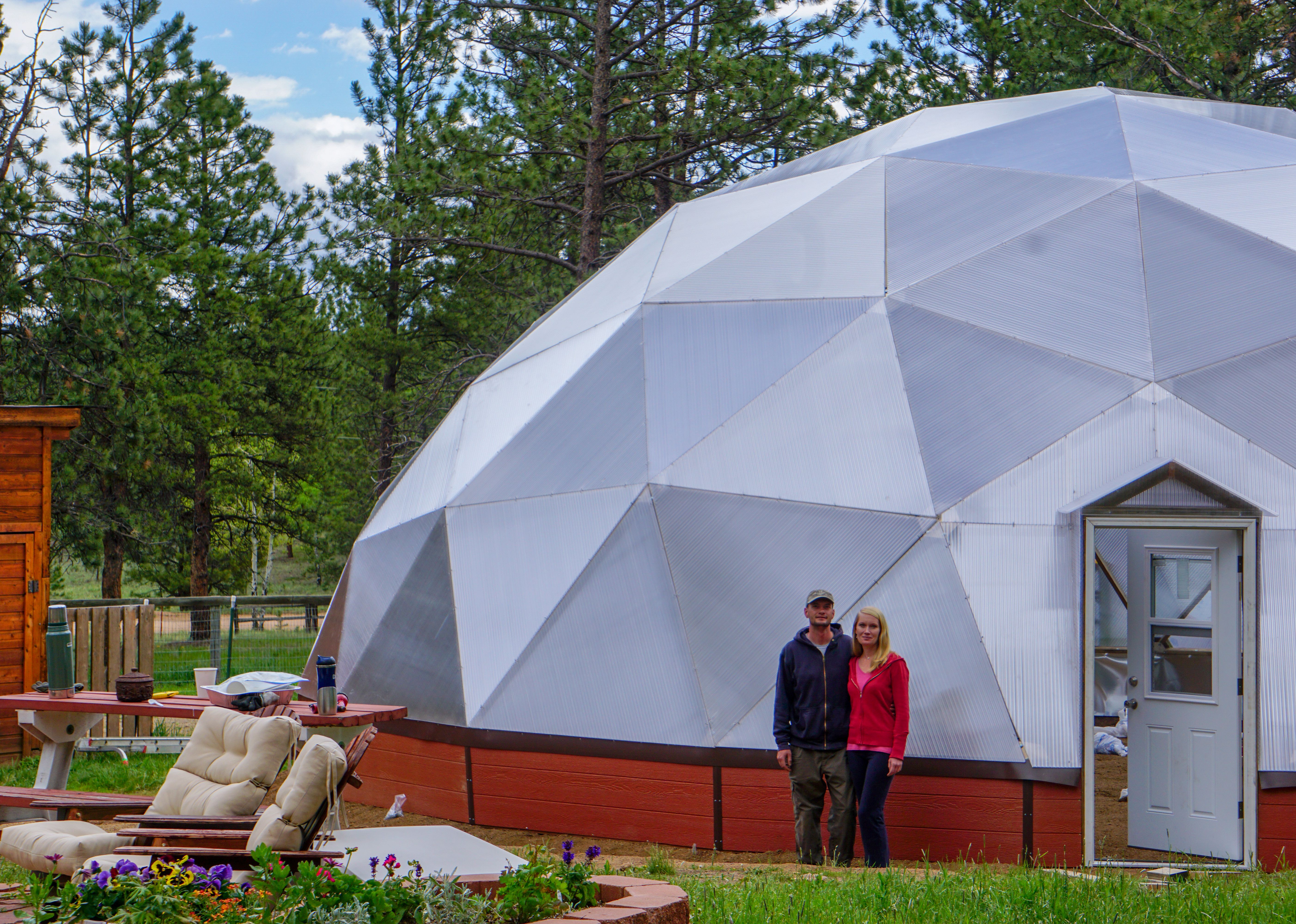 Man and woman standing in front of their 42 foot growing dome greenhouse