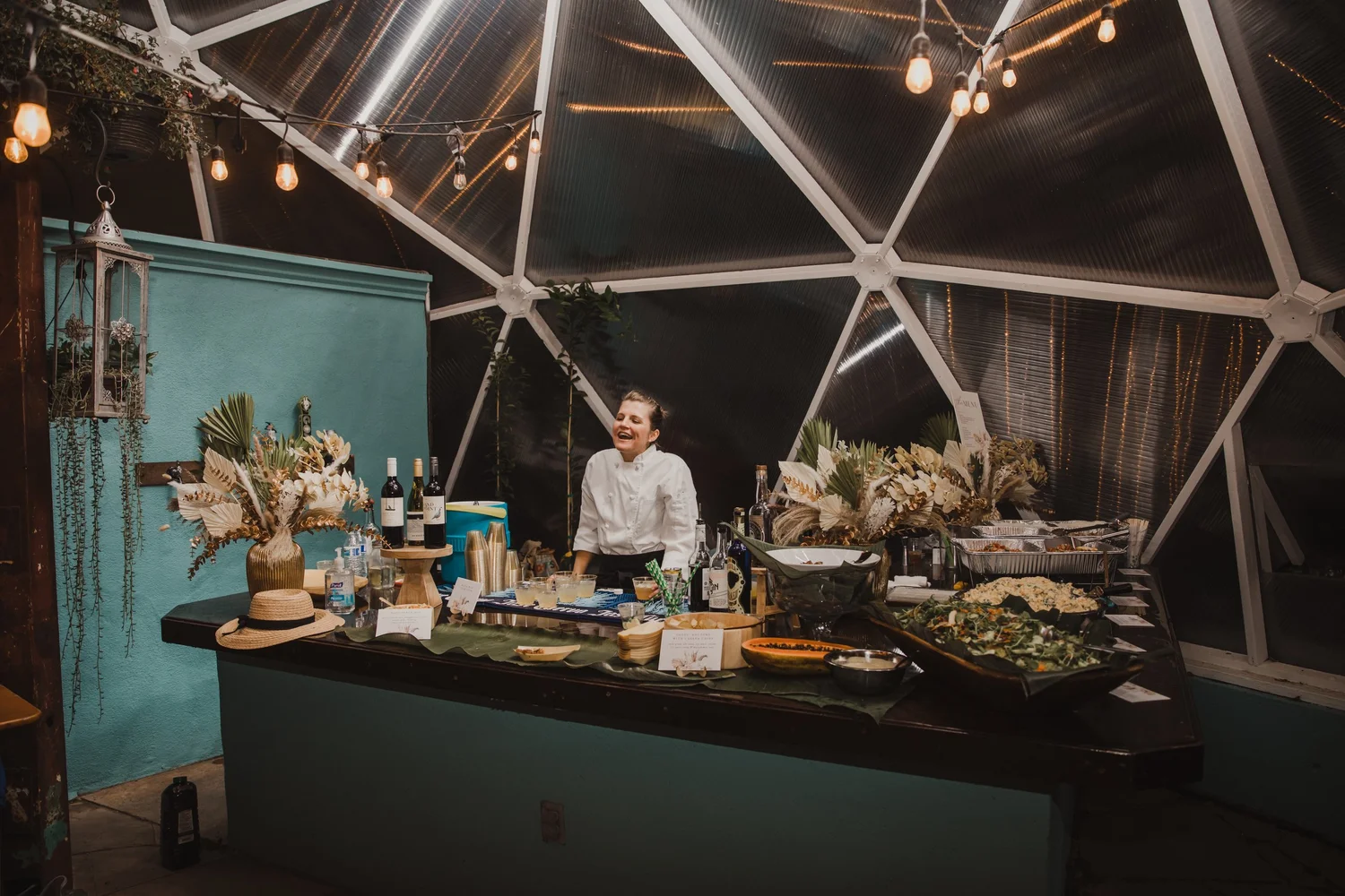 Bartender laughing inside a growing dome greenhouse bar with appetizers laid out