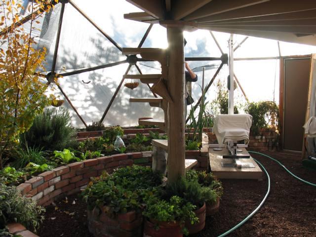 spiral staircase leading up to a deck looking at it from underneath with brick raised beds around the sides