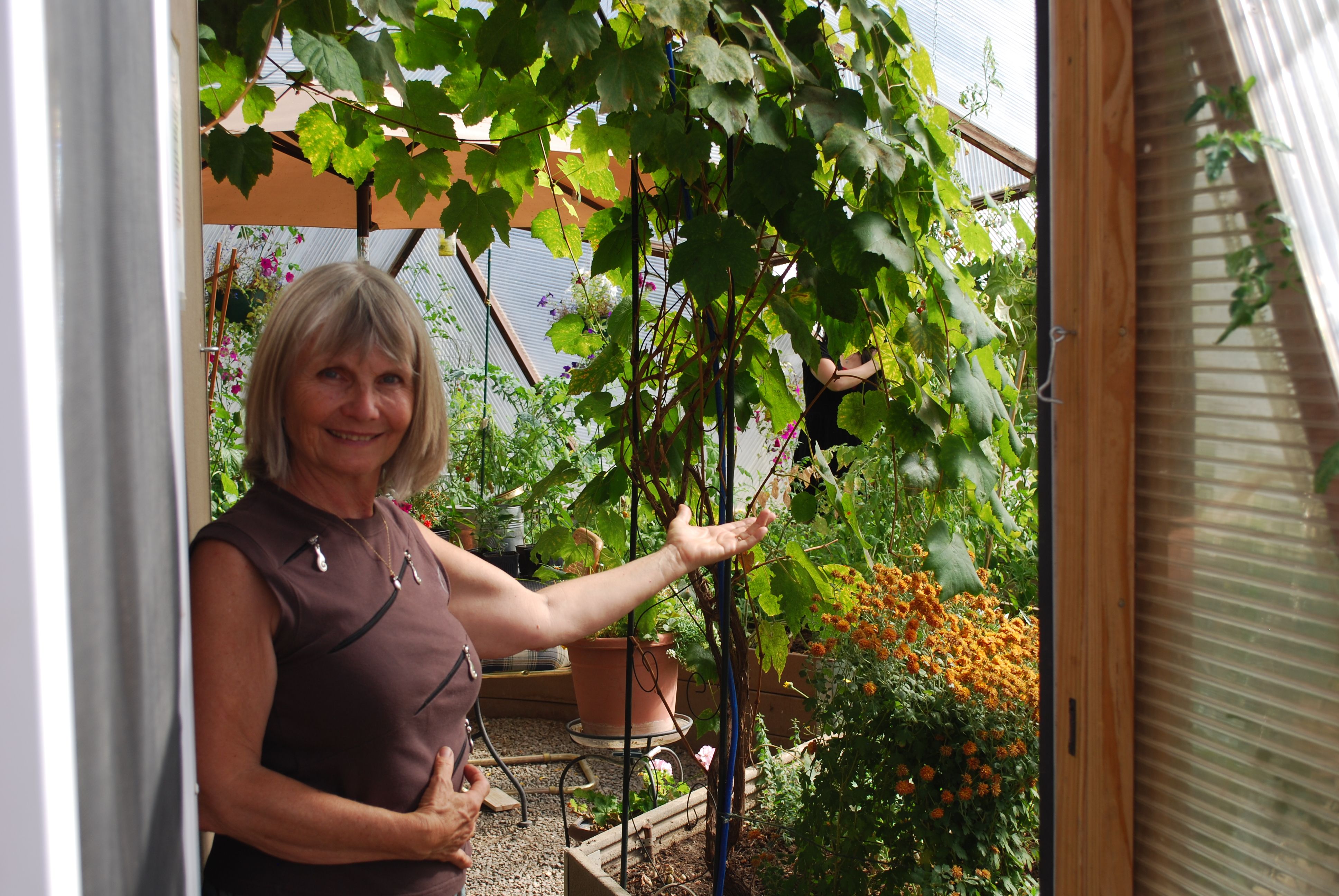 woman standing in the doorway inviting you in to explore the inside of the greenhouse