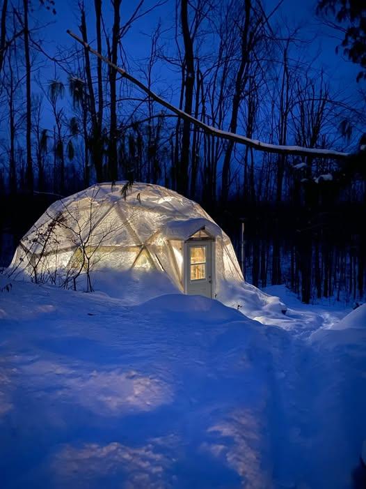 Khris and Allen Nedam's 26-foot Growing Dome glowing at night with snow piled outside in northern Michigan