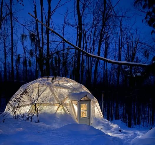 A 26-foot Growing Dome glowing at night with snow piled outside in Northern Michigan