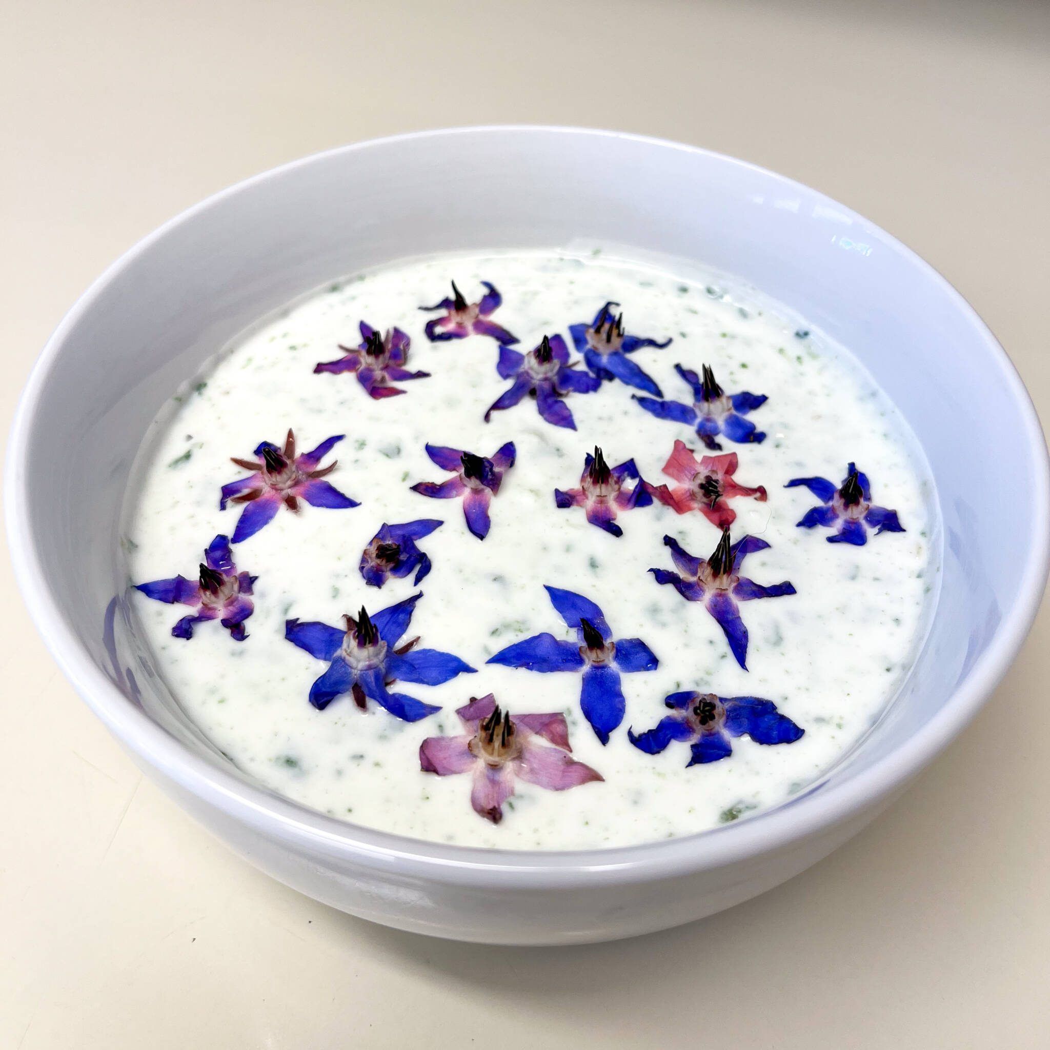 Borage Tzatziki in a bowl garnished with purple and pink borage blossoms