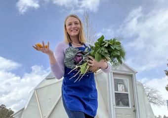 woman holding a bunch of freshly harvested greens standing outside a greenhouse