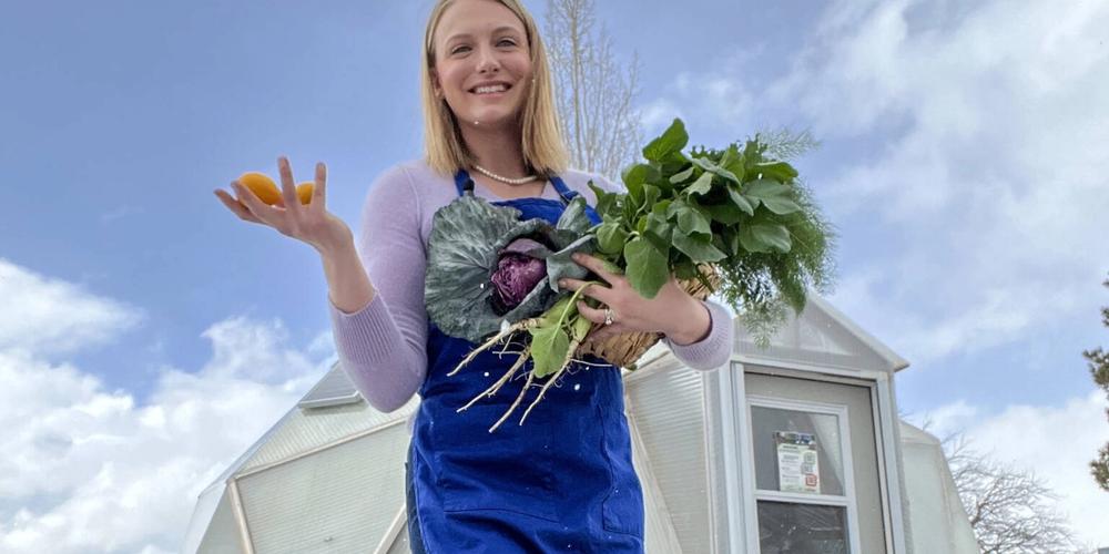 woman holding a bunch of freshly harvested greens standing outside a greenhouse