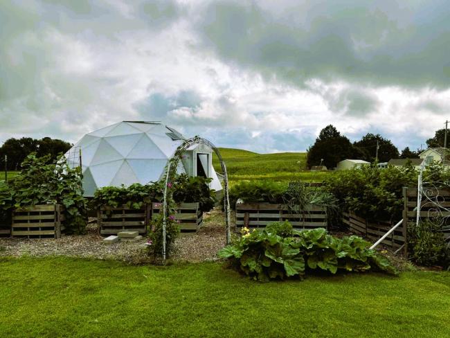 Dome greenhouse on a homestead with an outdoor garden and rolling green hills