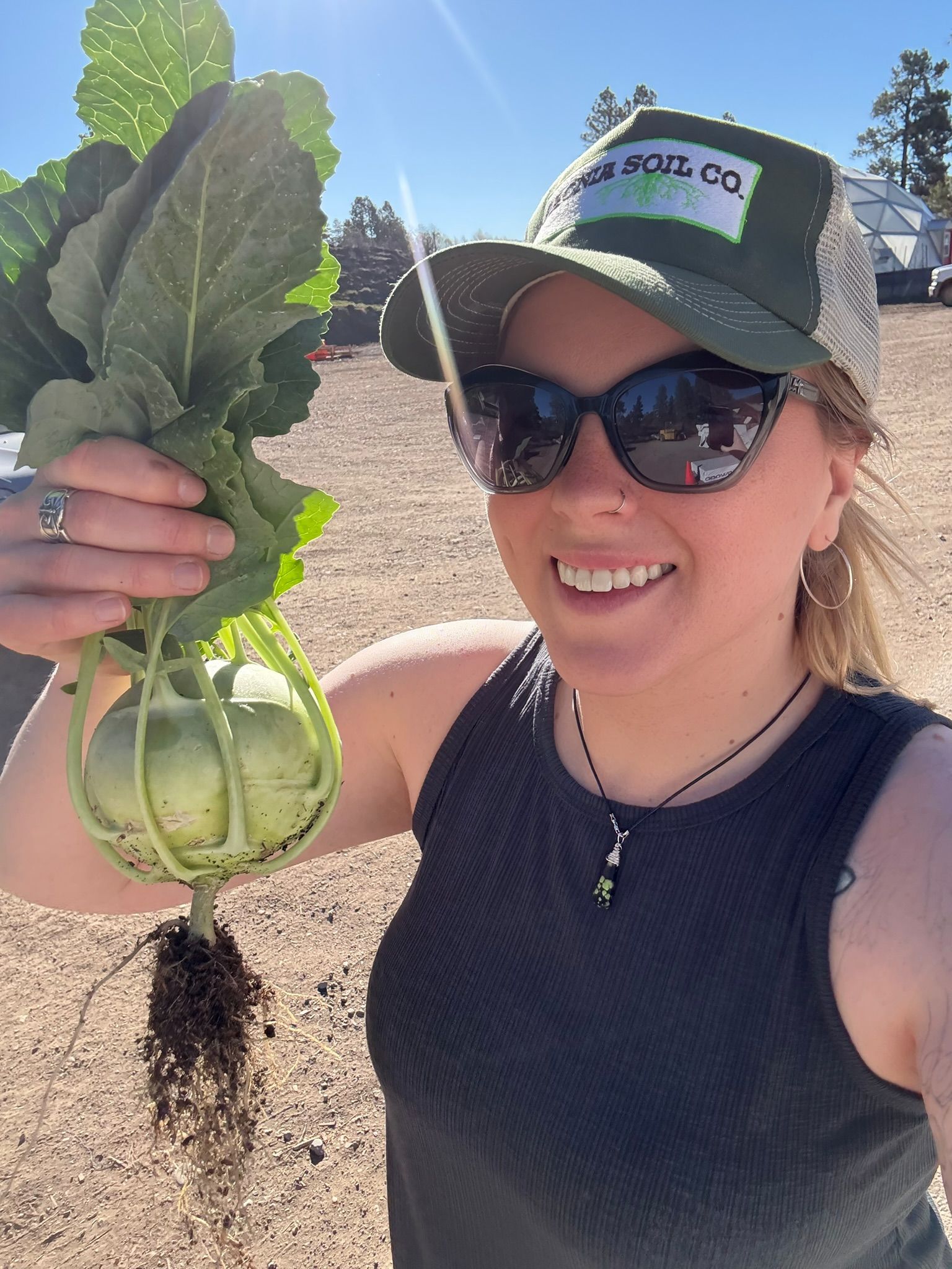 Woman in sunglasses holding a freshly picked kohlrabi with dirt still on the roots