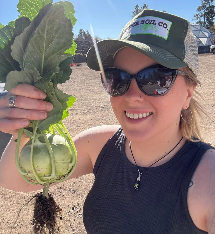 Woman in sunglasses holding a freshly picked kohlrabi with dirt still on the roots