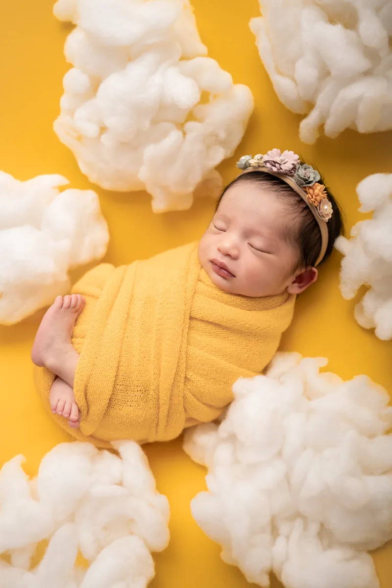 newborn sleeping among clouds with yellow background