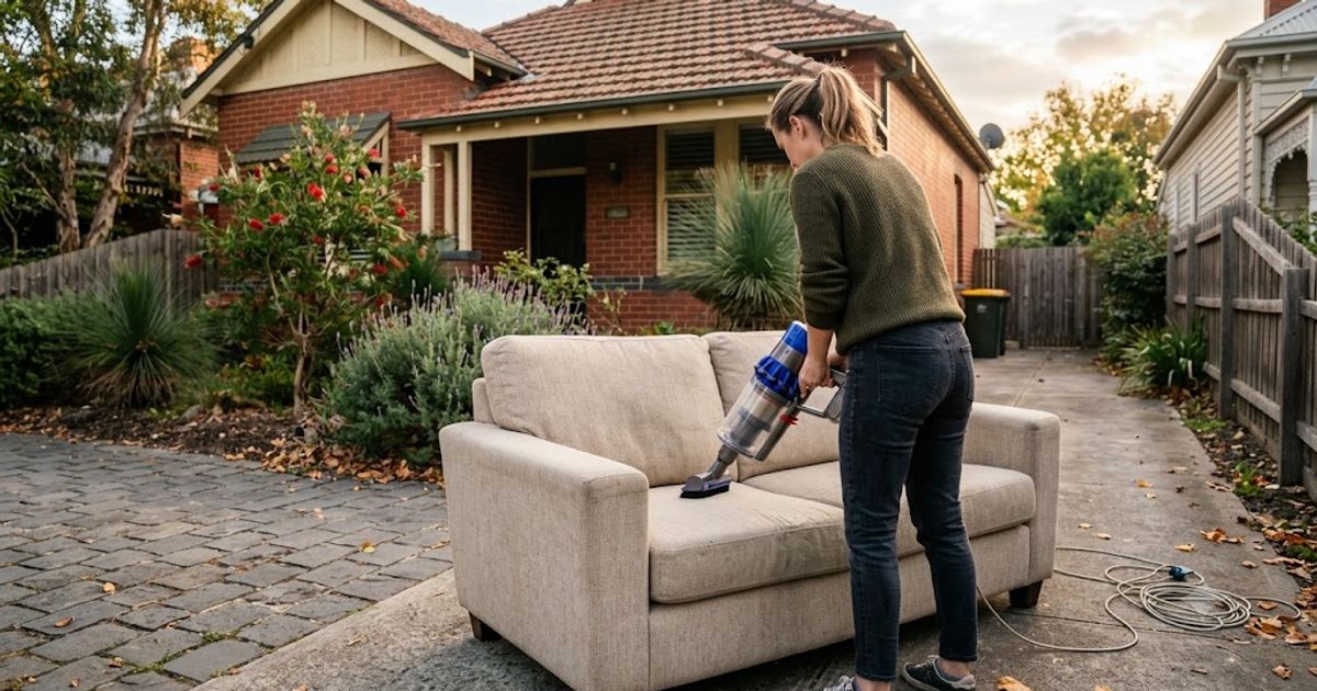 Person vacuuming a secondhand fabric sofa outside a Melbourne home before bringing it inside — how to clean used furniture