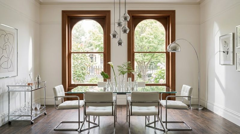 Chrome dining chairs with white cushions around a glass dining table and silver bar cart in a contemporary Melbourne apartment — cool metallics furniture trend 2026